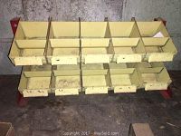 Full front view of the metal hardware keeper rack showing 12 yellow metal bins in two rows on a red metal frame.