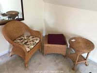 Wicker chair with floral cushion, rectangular foot rest with maroon cushion, and round wicker side table, all set on carpet