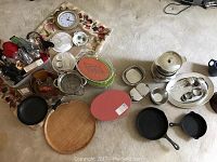 Overview of assorted serving dishes, cast iron pans, cutting board, glass bowls, utensils and a clock.