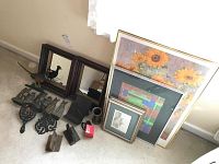 Lot of wooden framed mirrors, framed prints, metal bookends, and trivets arranged on carpeted floor near window and wall with curtain.