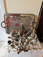 Full view of silverplate tray with assorted silverplate and nickel cutlery and serving pieces scattered in front.