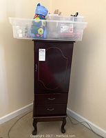 Wooden jewelry chest standing with various plastic bins on top holding ceramic figurines and doll parts.