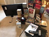 27-inch Vizio TV, multiple VHS tapes and DVD boxed sets stacked around and in front of the TV