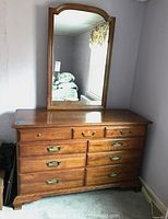 Full view of wooden dresser with attached mirror, placed against wall, showing overall structure and finish.