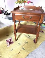 Photo showing the wooden end table with drawer and lower shelf, standing on the floral-patterned rug.