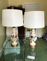 Pair of 26-inch tall ceramic lamps with white drum shades, placed on glass table in room setting.