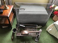 Photo showing the wrought iron fireplace grate with tools and boot holder near a grey ottoman