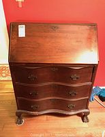 Front view of vintage 1940s secretary desk closed showing curved drawer fronts, brass hardware, and claw feet.