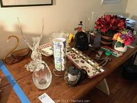 Wide view of assorted glassware, decorative trays, artificial flowers, and clock radio on table.