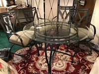 Full view of 45-inch round beveled glass top table with metal base and four metal chairs around it on a floral patterned rug.