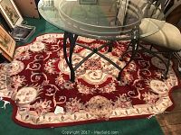 Full view of a deep red oriental floral pattern rug under a glass table, showing scalloped ends.