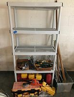 Full view of white plastic shelving unit holding multiple toolboxes, hand and power tools, and some garden tools to the side in a translucent container.