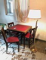 Card table with three matching chairs and standing floor lamp shown in room setting with floral rug and striped curtains.