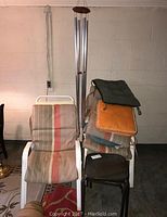 Photo of two white metal outdoor chairs with beige, red, and orange striped cushions; metal wind chimes in the background; assorted cushions piled on chair and floor; small metal table visible.