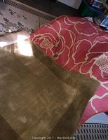 Photo showing two rugs: a beige and white outdoor rug with wear and a bright orange floral pattern rug folded on top.