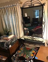 Black wrought iron framed mirror with swirling decorative accents, mounted above matching wrought iron shelf with mirrored top in room corner.