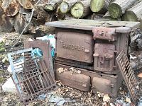 Overall view of the vintage cast iron wood burning stove and oven showing embossed 'THATCHER' on front, removable cast iron grate, and rusted condition.