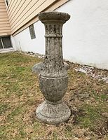 Tall concrete pedestal standing on grass, textured surface, showing outdoor weathering.