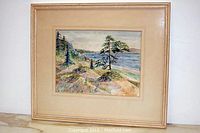 Framed watercolor painting showing landscape including a lake, trees, rocks, and small wooden structure.