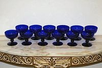 Front view of all 12 cobalt blue glass dessert cups arranged in a row.