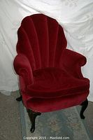 Full front view of red velvet armchair on rug with draped backdrop