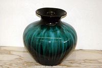Front view showing bulbous shape and blue-green drip glaze with pinched neck design.