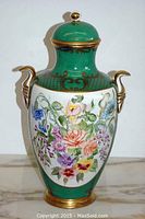 Front view of green porcelain urn with floral painting, gold handles, base and trim.