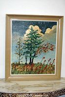 Framed oil painting depicting impressionist style trees with clouds in the background, positioned on a marble surface.