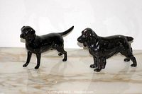 Two black porcelain dog figurines on marble surface, front and side views