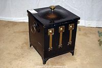 Front angle view showing the coal scuttle with three vertical brass handles on the front and brass ring handles on the sides, resting on decorative feet.