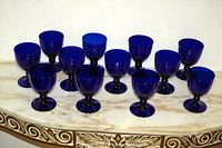 12 cobalt blue wine/water glasses arranged in two rows on a marble surface.