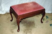 Front angle view of antique walnut bench with pink velvet upholstery and carved legs.