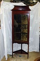 Front view of mahogany corner cabinet showing pediment top, glass door, velvet interior.