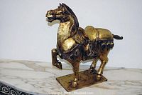 Side view showing the gilded carving of the horse with raised front leg, saddle detail, and rectangular base.