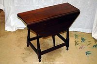 Side view of table with one leaf folded down and one leaf extended, showing gateleg supports.