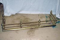 Full view of the antique brass fireplace surround showing overall shape and design on floor with a white backdrop.