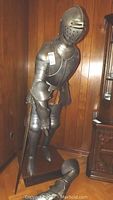 Full front view of life-size knight armor on wooden pedestal with left gauntlet and sword detached at base