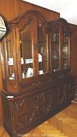 Front view of the two-piece china cabinet showcasing arched double glass doors, carved accents, and display of china inside.
