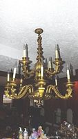 Full view of vintage brass tone chandelier with ornate Rococo details hanging from ceiling, showing all 12 candle lights on two tiers.
