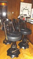 Four dark stained wooden swivel bar stools with round black padded seats arranged on parquet floor