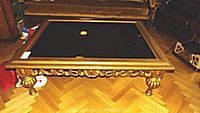 Full view of the coffee table showing the black glass top and giltwood detailed carved legs and frame.
