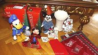 Photo showing Disney wind-up toys (Mickey Mouse & Donald Duck), Clothtique Santa figurines in red boxes, a white Lenox vase figurine, and holiday placemats and napkin.