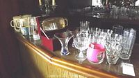 Wide view of the glassware collection including stemware, mugs, and candleholder on a wooden surface.