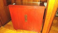 Closed front view of red wooden cabinet with glass top and brass handles