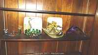 Ceramic wall plates and assorted art glass displayed on a wooden shelf