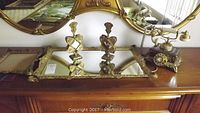 Gold tone mirrored tray with one broken corner and pair of ornate amber glass fragrance bottle holders on a dresser in front of a decorative mirror.