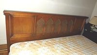 Full view of large wooden headboard with cane panels shown above a mattress, showcasing five arched cane inserts within a solid wood frame.