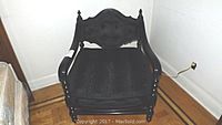 Front angled view of the black painted solid wood armchair with padded tufted back and cushion seat showing shape, upholstery, and wood details.