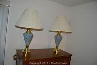 Two brass tone lamps with swirled ceramic bodies and pleated shades placed on wooden surface