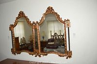 Front view of large double wall mirror with ornate giltwood frame mounted on wall above wooden dresser.